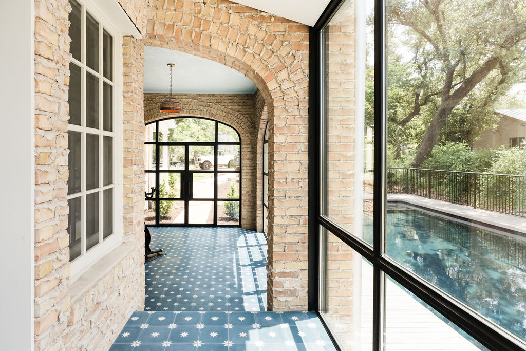 Sun room in Travis Heights historic home remodel with beige brick walls, blue and white tile floors, and lots of windows.