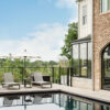 Exterior of Travis Heights historic home renovation with a new pool, lounge chairs and umbrellas, black metal fence, and black metal arched French doors.